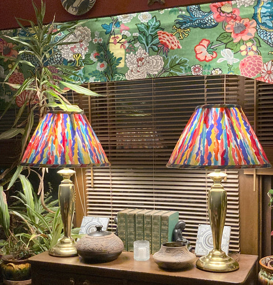 Stiffel lamps with colorful lampshades sitting on a dresser with books and pottery, in front of a window with a valance made in Schumacher's Chiang Mai Dragon fabric
