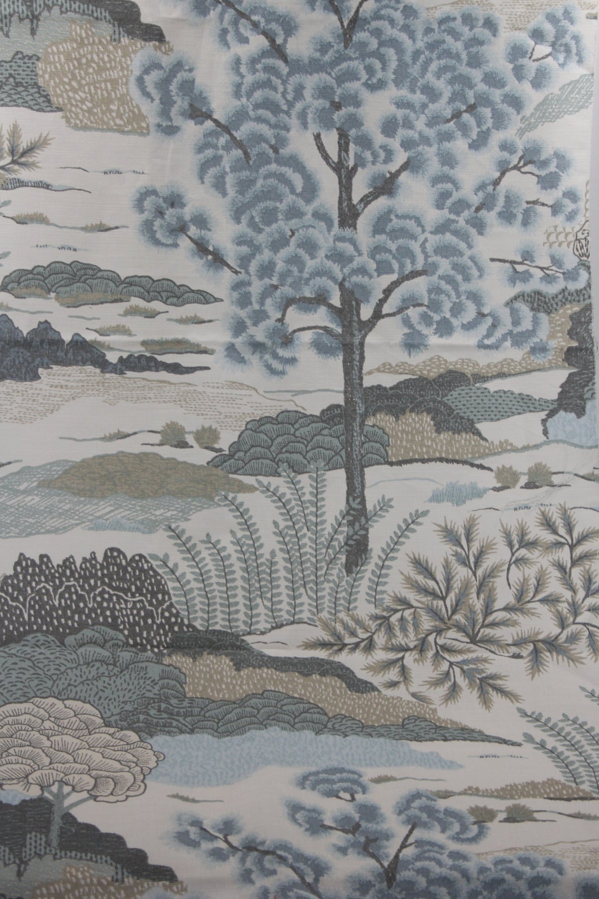 Flat lay of Thibaut's Daintree fabric showing entirety of design, with a large Japanese pine rendered in soft blues and set in a landscape of shrubs, dunes, and hills in blues, teals, and browns